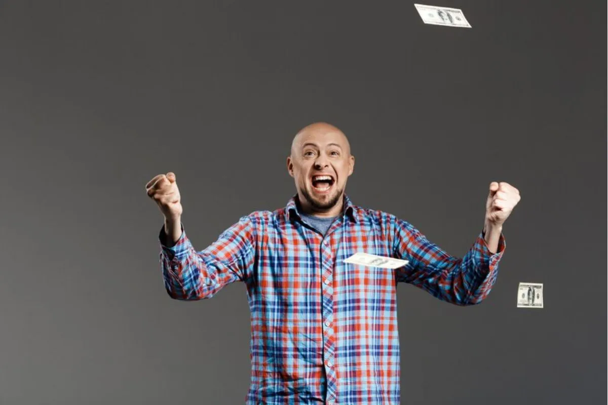 Homem comemorando conquista de loteria com bilhetes caindo do teto.