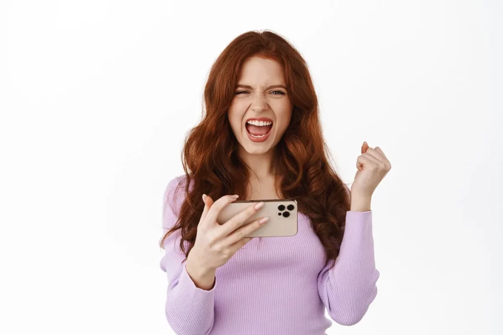 Mulher animada segurando um smartphone enquanto comemora, representando emoção ao usar um sorteador de números.