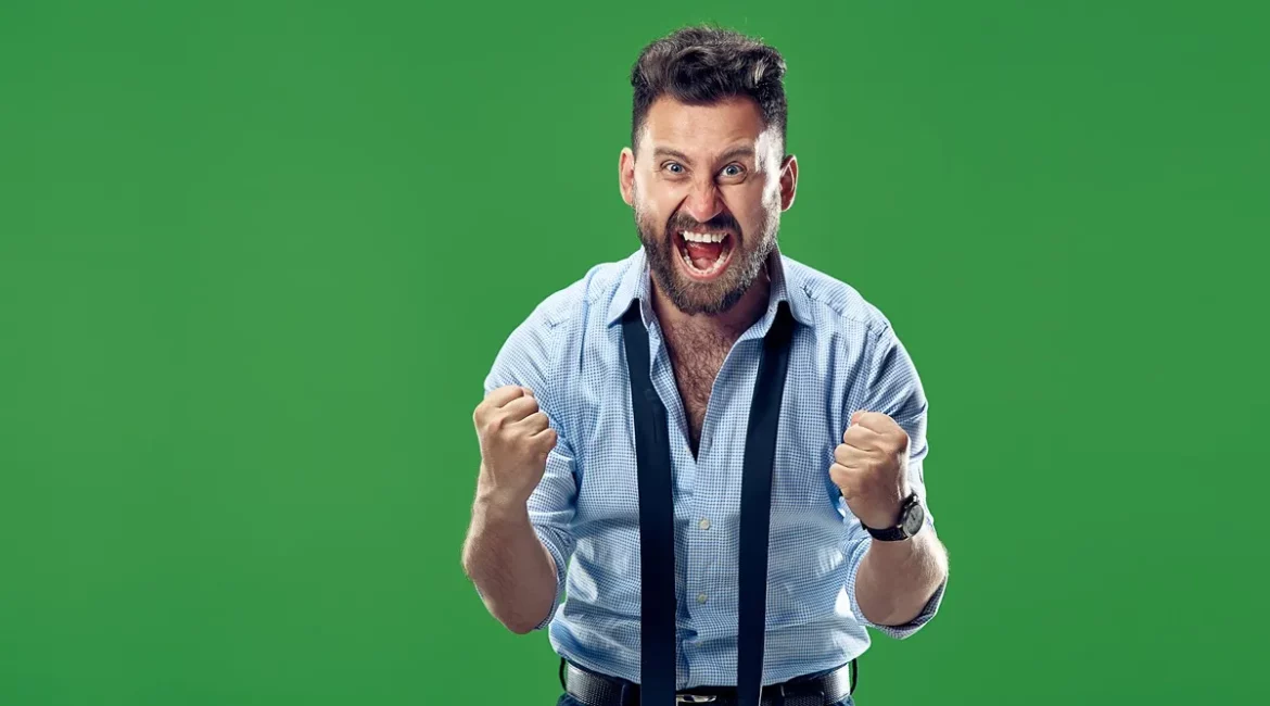 Homem com expressão de felicidade intensa, vestindo camisa social e gravata solta, comemorando com os punhos cerrados, em frente a um fundo verde.