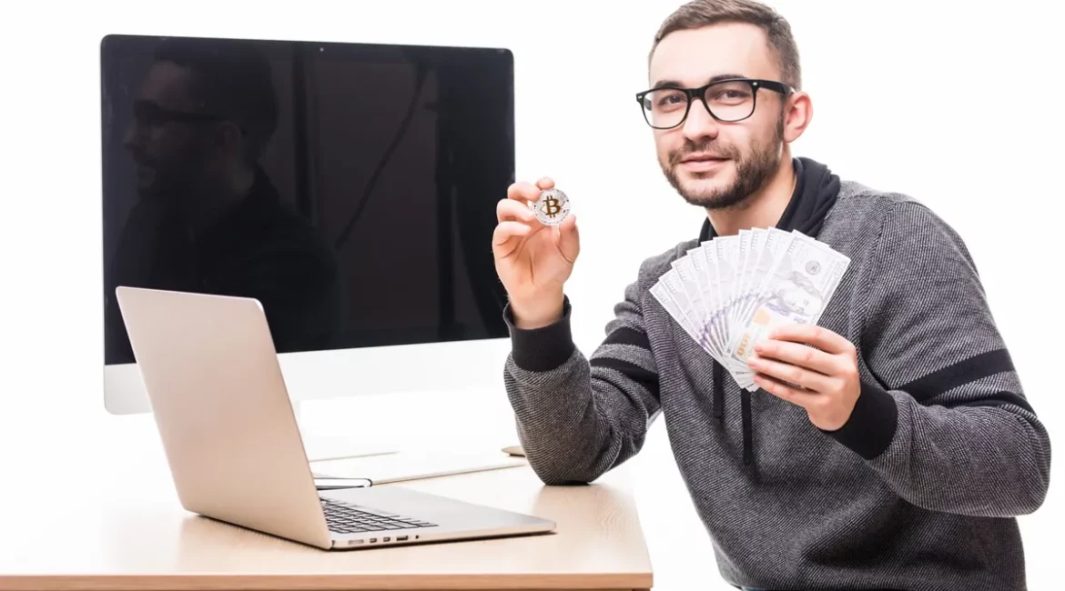 Homem com óculos segurando um leque de notas de dólar e uma moeda de Bitcoin, representando investimento em criptomoedas e transações financeiras online